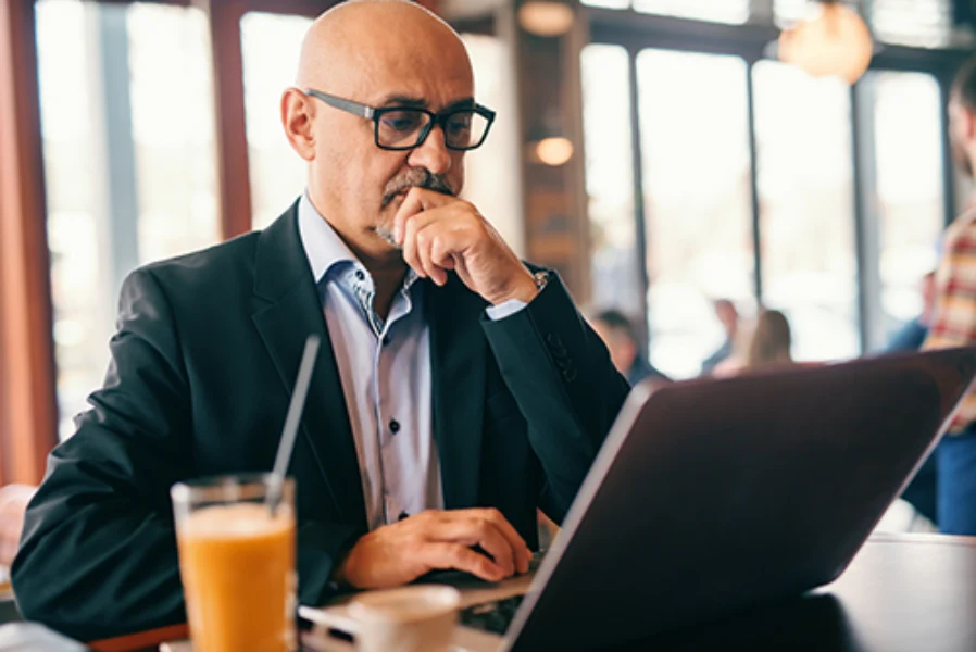 Mature Man Wearing Designer Prescription Glasses Working On A Laptop