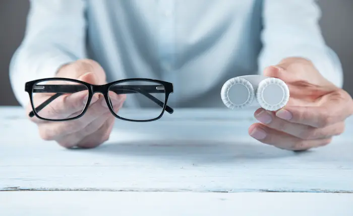 Contact Lenses Vs Glasses – Which Is Right For You? 1 Contact Lenses Vs Glasses Comparison Showing Hands Holding Eyeglasses And A Lens Case.