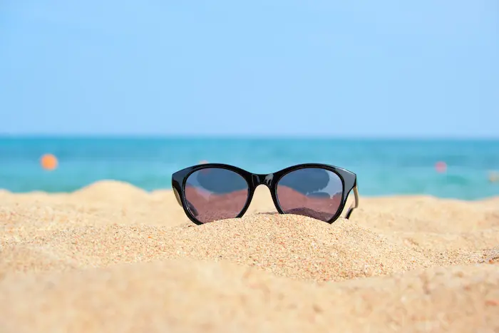 Best Uv Protection For Eyes: Protecting Your Eyes From Uv Rays 7 Uv Protection For Eyes – Sunglasses Resting On Sandy Beach With Ocean In Background.